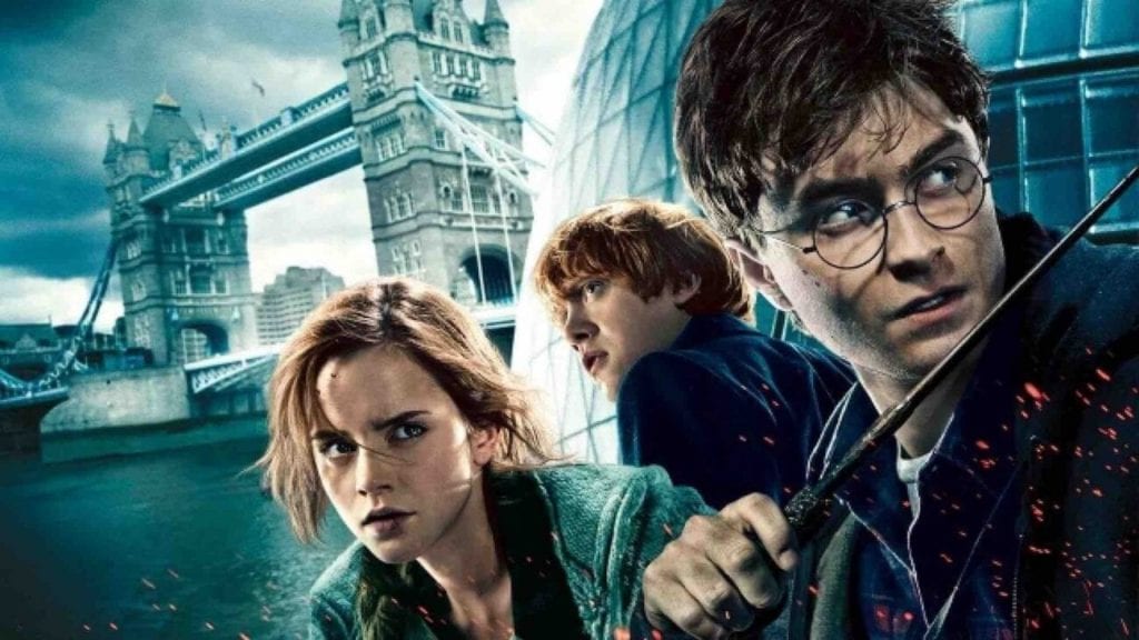 Two boys, one holding a wand, and a girl are in front of Tower bridge in London, all looking dramatically away from the camera