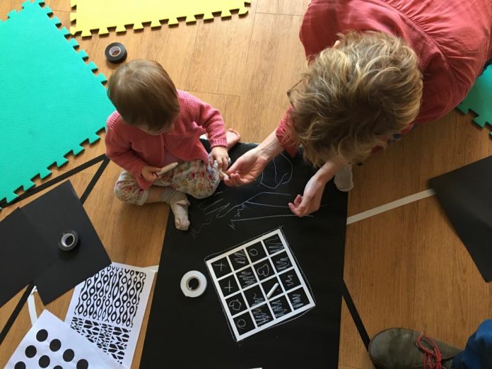 An image from one of Spun Glass Theatre's previous workshops. A child is drawing on a chalkboard with help from an adult